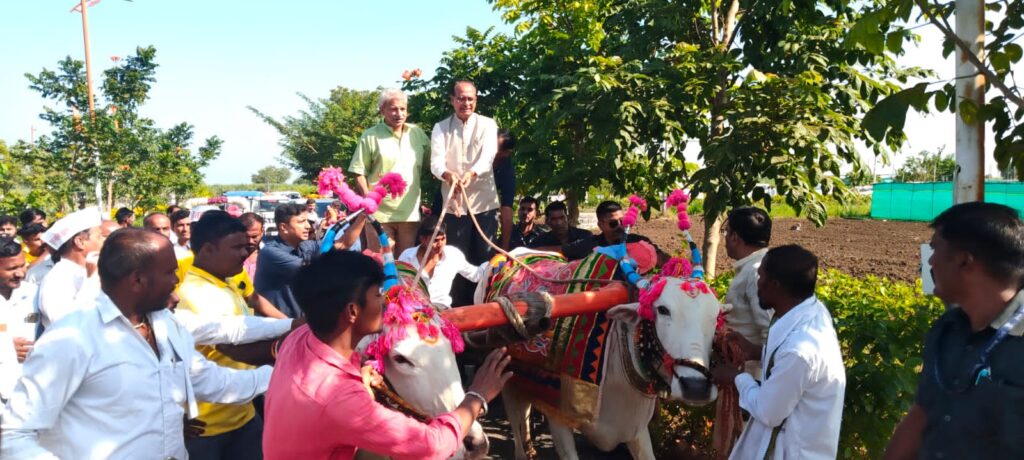 Union Agriculture Minister Shri Shivraj Singh Chouhan standing on a bullock cart, addressing a large conference of farmers in rural Maharashtra under a clear sky. The cart is adorned with colorful decorations, and many farmers are gathered around, listening attentively.