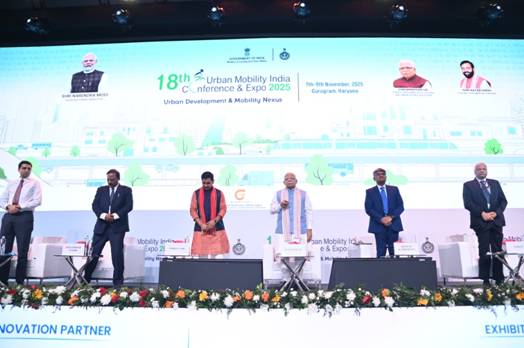 Union Minister Shri Manohar Lal inaugurating the 18th Urban Mobility India (UMI) Conference & Exhibition 2025 in Gurugram. The image shows several dignitaries on a stage with a large screen behind them displaying the event logo and other information.