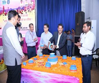 Men pouring water from small pots into a larger central pot on a flower-decorated table during a ceremonial event with a banner in the background.