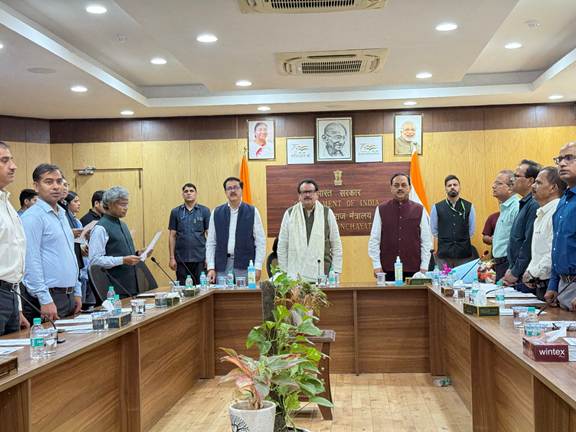 A group of Indian officials, mostly men, standing in a meeting room with portraits on the wall, commemorating 150 years of Vande Mataram.