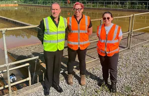 Three individuals in high-visibility vests standing in front of water treatment basins.