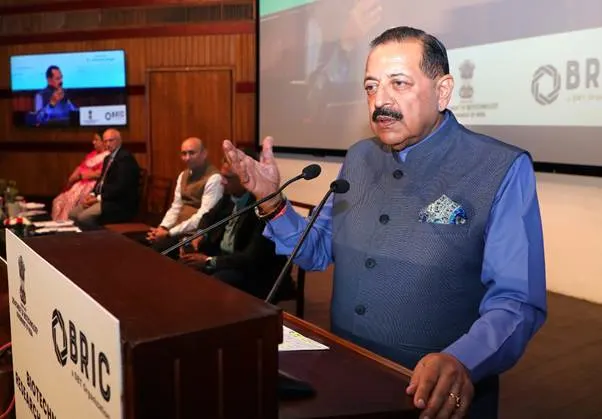 Union Minister Dr. Jitendra Singh speaking at a podium with a microphone, gesturing with his right hand, in front of an audience with "OBRIC" and "BIOTECH RESEARCH" visible on the podium and screens in the background.