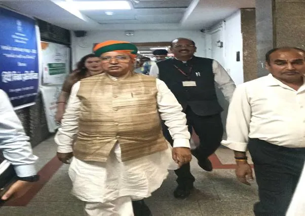 A man in traditional Indian attire, including a turban and a vest over a kurta, walks through a brightly lit indoor corridor, flanked by other men.