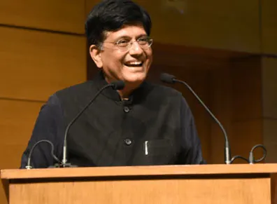 Union Minister Piyush Goyal smiling while speaking into microphones from a wooden podium at a conference or event.