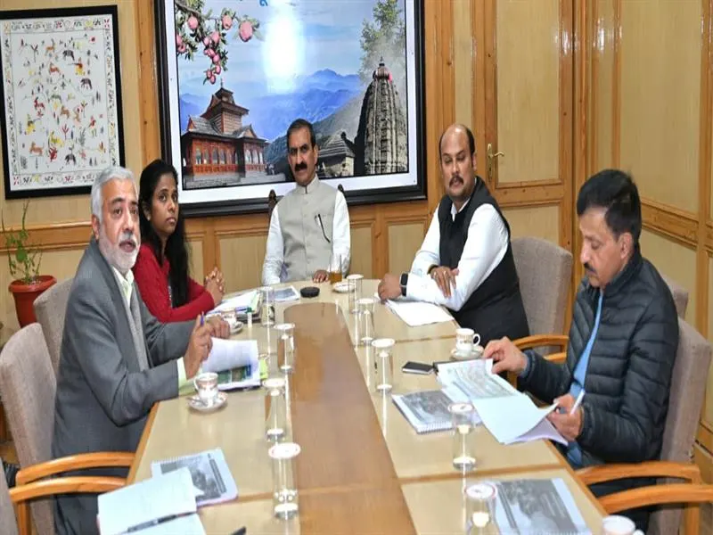 A group of five government officials, including one woman, sitting around a conference table during a review or planning meeting in an office setting.
