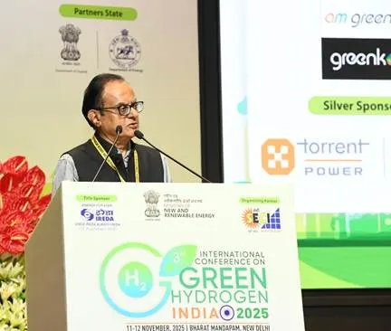 A man in glasses and a dark vest speaks at a podium with "INTERNATIONAL CONFERENCE ON GREEN HYDROGEN INDIA 2025" visible on the front.