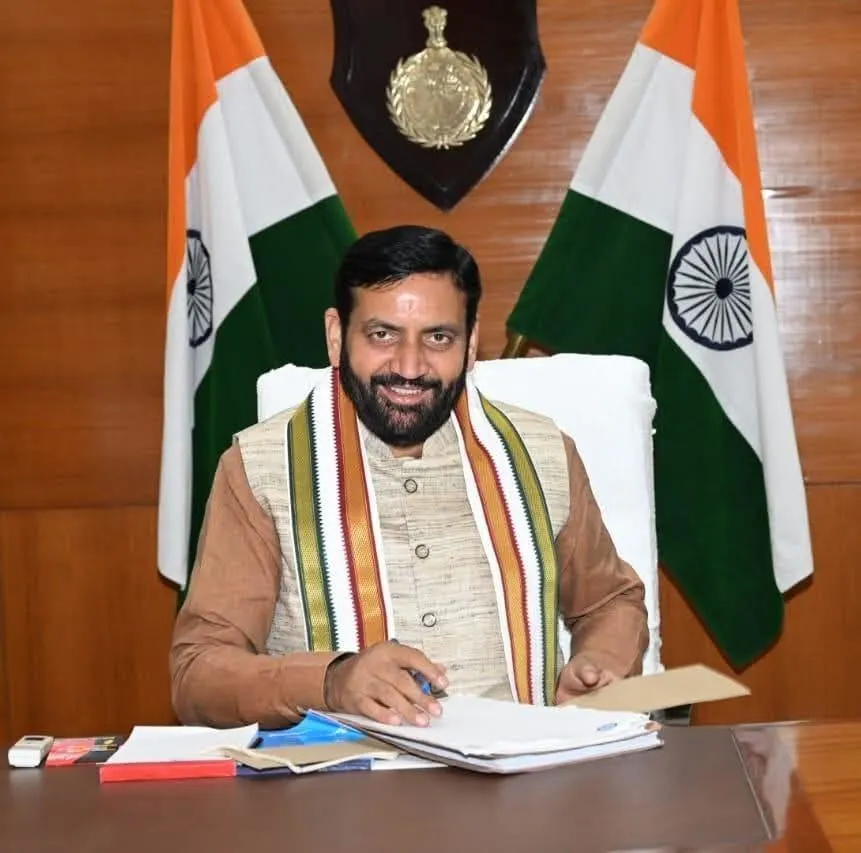 Nayab Singh Saini, Chief Minister of Haryana, smiling while seated at his official desk with documents and the Indian national flag in the background.