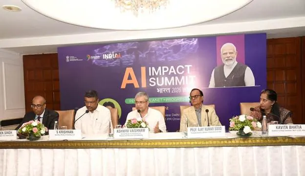 Five individuals seated at a long table with microphones and floral arrangements, in front of a large banner for the "AI IMPACT SUMMIT Bharat 2023." The banner features images of Prime Minister Narendra Modi and text related to AI.