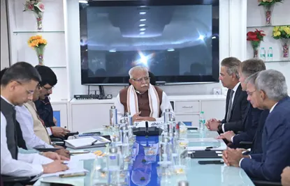 Group of men in business attire seated around a large conference table, with one man in traditional Indian attire speaking.
