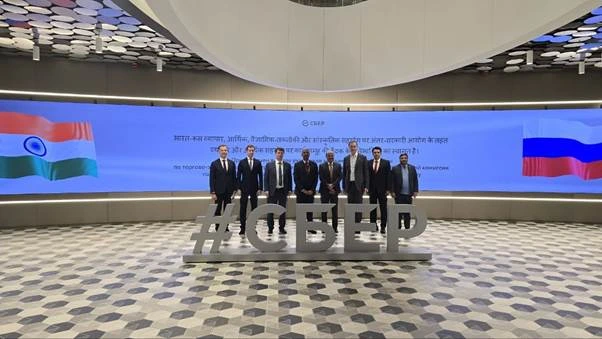 Group of nine men in suits standing in front of a large screen displaying the Indian and Russian flags, with text in Hindi and English, and a large #SBER sign in the foreground.