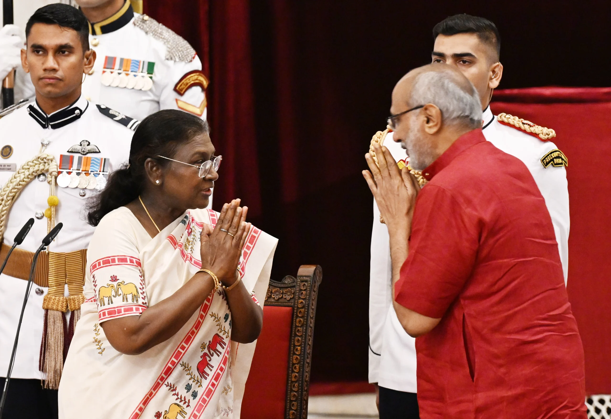 Droupadi Murmu, the President of India, greets a man with a namaste gesture, as he reciprocates the gesture, with uniformed personnel in the background.