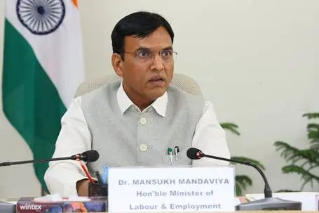 Union Minister Mansukh Mandaviya speaking at a desk with microphones and the Indian flag in the background.