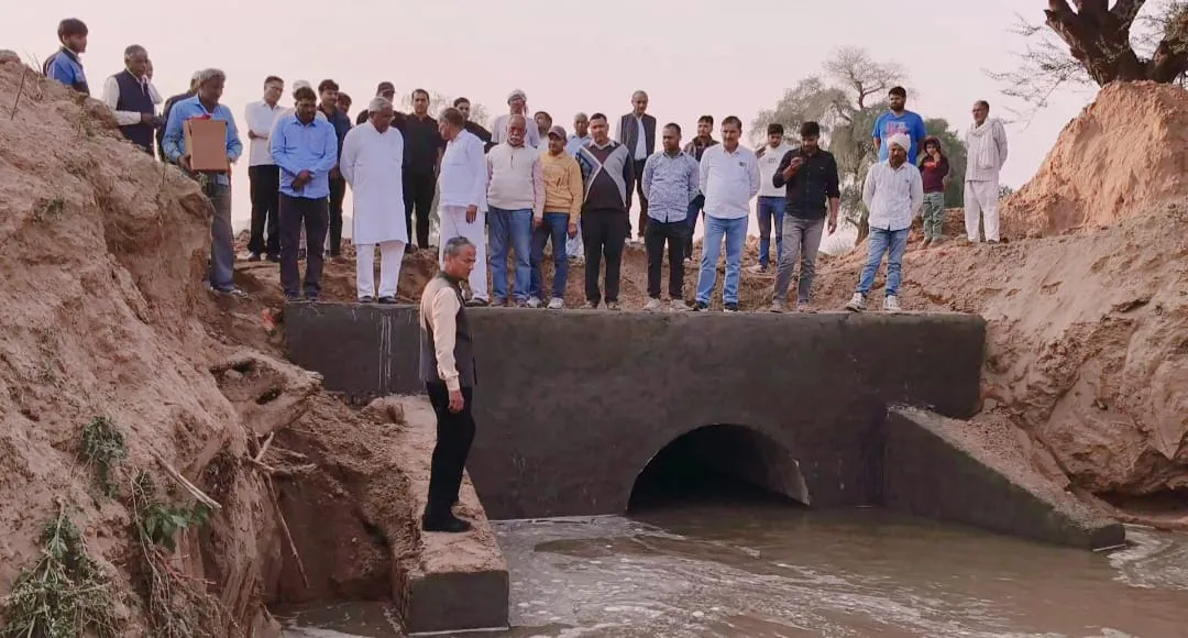 हरियाणा के नारनौल/अटेली-कनीना क्षेत्र में कृष्णावती नदी रिचार्ज लाइन के नए बने पुलिया पर पूर्व विधायक सीता राम यादव और पूर्व सिंचाई मंत्री डॉ. अभय सिंह यादव (अग्रभूमि में) ग्रामीणों व अधिकारियों के साथ पानी के प्रवाह का निरीक्षण करते हुए। संरचना के नीचे से पानी बह रहा है, और आसपास सूखी मिट्टी के टीले हैं।