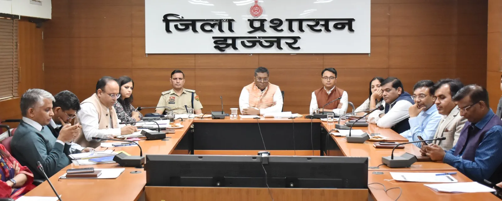 झज्जर जिला प्रशासन की एक बैठक, जिसमें डीसी स्वप्निल रविन्द्र पाटिल और अन्य अधिकारी कॉन्फ्रेंस हॉल में यू-आकार की मेज के चारों ओर बैठे हैं। पीछे "जिला प्रशासन झज्जर" का बोर्ड लगा है।