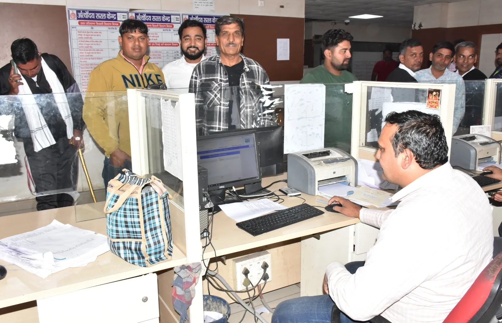 अंत्योदय सरल केंद्र के काउंटर पर एक सरकारी कर्मचारी कंप्यूटर पर काम कर रहा है, जबकि कई नागरिक (आवेदक) सेवा लेने के लिए शीशे की पार्टीशन के पीछे खड़े हैं। पीछे "अंत्योदय सरल केंद्र" के बोर्ड और सूचनाएं दिख रही हैं, जो पेपरलेस रजिस्ट्री हेल्पडेस्क की त्वरित सहायता को दर्शाती हैं।