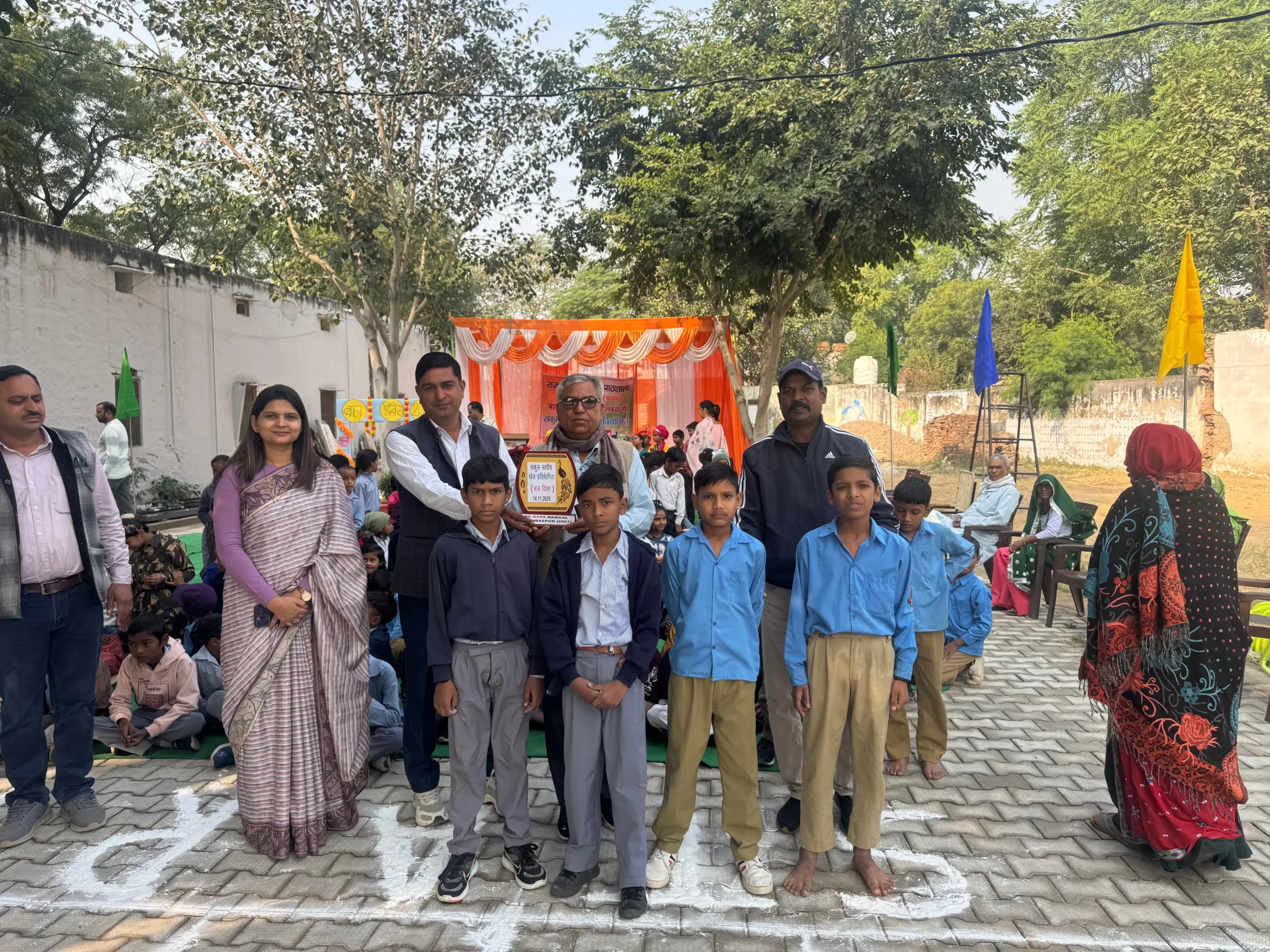 राजकीय प्राथमिक पाठशाला नांगल शहबाजपुर में बाल दिवस समारोह के दौरान जिला परियोजना अधिकारी राजेंद्र शर्मा और अन्य अधिकारी/शिक्षक स्कूल स्तरीय प्रतियोगिता के विजेताओं (छात्रों) को शील्ड प्रदान करते हुए।