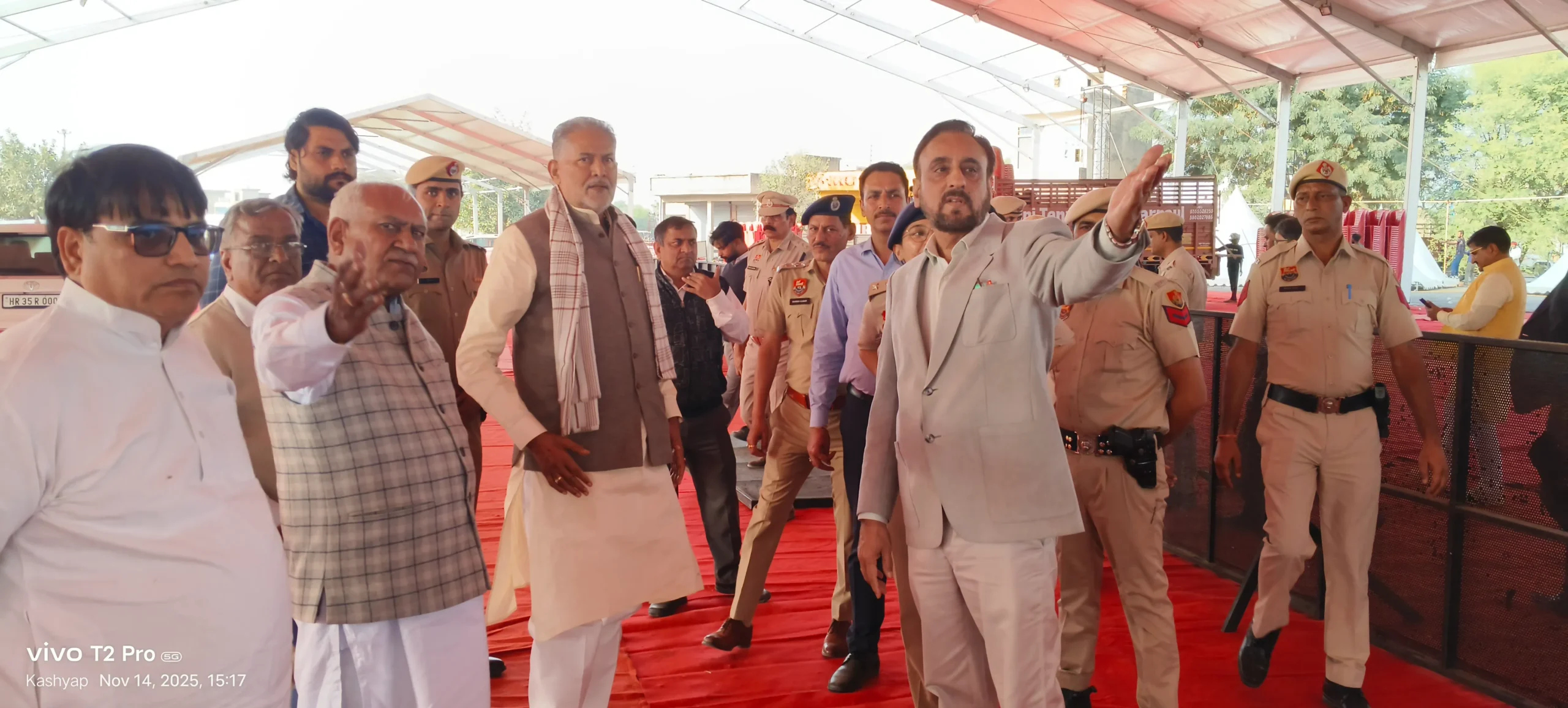 नारनौल के विधायक और पूर्व मंत्री ओम प्रकाश यादव (भूरे रंग की सदरी और सफेद-लाल चेकर्ड दुपट्टा पहने) और एक अन्य नेता (हल्के बेज रंग के सूट में, हाथ उठाकर निर्देश देते हुए), पुलिसकर्मियों और अधिकारियों के साथ नारनौल की नई अनाज मंडी में महाराजा शूर सैनी जयंती समारोह की तैयारियों का जायजा लेते हुए।