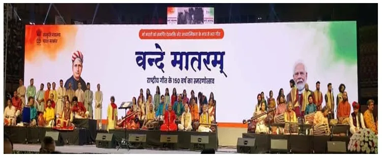 A large stage setup with a white backdrop displaying "Vande Mataram" in Hindi, flanked by portraits of Bankim Chandra Chatterjee and Prime Minister Narendra Modi, with three groups of musicians and vocalists performing traditional Indian music.