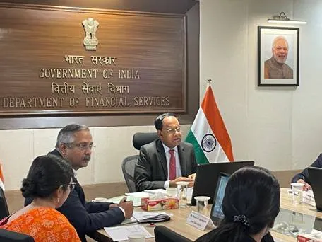 Close-up of Shri Vivek Joshi, Secretary of the Department of Financial Services (DFS), Government of India, addressing participants during a webinar. He is seated at a conference table with an Indian flag to his right and a framed portrait of Prime Minister Narendra Modi on the wall behind him. Other officials are partially visible around the table, listening.