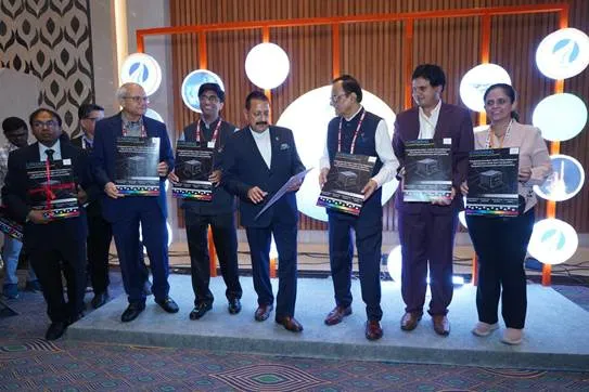 Seven individuals, six men and one woman, stand on a raised platform holding plaques or certificates, suggesting an award ceremony or book launch, against a backdrop of modern, illuminated geometric shapes.