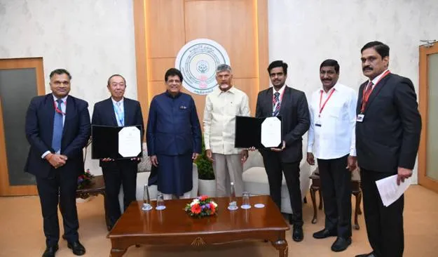 A group of seven men, including Andhra Pradesh Chief Minister N. Chandrababu Naidu, pose for a photograph after signing agreements. Naidu, in a light yellow shirt, stands prominently in the center. To his left, three men in dark suits hold up white documents in black folders. To his right, two men in a dark suit and a white shirt also hold up similar documents. The men are standing in a well-lit room with a wooden table in the foreground and a circular emblem on the wall behind them.