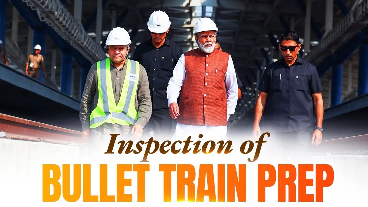 Indian Prime Minister Narendra Modi, wearing an orange waistcoat over a white kurta, walks with a group of men in hard hats and safety vests on what appears to be a bullet train track. One man in a yellow-green vest walks beside him, while security personnel in dark suits flank them. The setting is an industrial or construction site, likely for the bullet train project, with metal structures visible in the background.