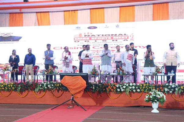A group of male dignitaries stand on a raised stage with a large banner behind them at the 4th National EMRS Sports Meet 2025 closing ceremony in Rourkela.