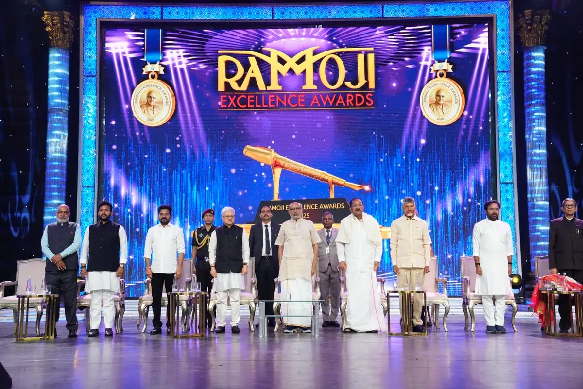 Dignitaries including the Vice-President of India, Chief Ministers, and Union Ministers stand on a stage with a large LED screen displaying 'Ramoji Excellence Awards 2025' and a golden pen trophy. The stage is brightly lit with blue and purple lights. From left to right: Shri G. Kishan Reddy, Shri Ch. Kiron, Shri Srikant Bolla, an army officer, Shri Jishnu Dev Varma, Shri C. P. Radhakrishnan, Shri M. Venkaiah Naidu, Shri N. Chandrababu Naidu, Shri A. Revanth Reddy, and Shri N. V. Ramana.