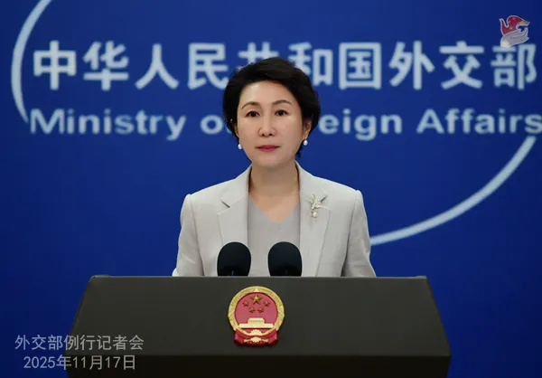 Chinese Foreign Ministry Spokesperson Mao Ning standing at a podium with microphones, delivering a press conference. She is wearing a light-colored suit jacket over a grey top, with a pin on her lapel. Behind her is a blue backdrop with the official seal and the words 'Ministry of Foreign Affairs' in English and Chinese characters.