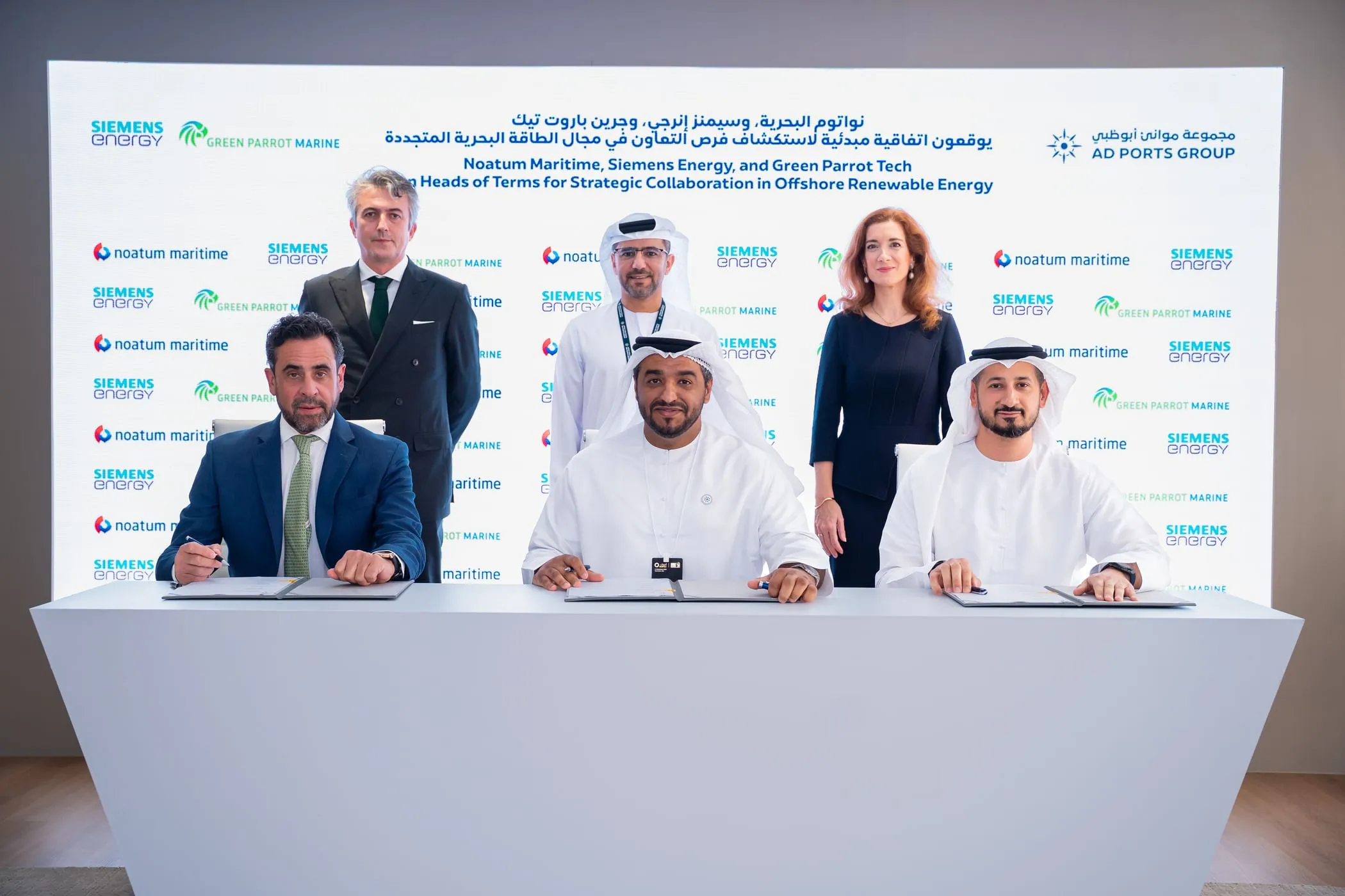 Six executives from Noatum Maritime, Siemens Energy, and Green Parrot Tech pose for a group photo after signing a strategic collaboration agreement in Abu Dhabi. Three executives are seated at a table with signed documents, while three others stand behind them. A large white backdrop with company logos and Arabic and English text about the partnership is visible.