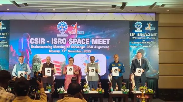 Seven individuals, including scientists, astronauts, and international experts, stand on a stage holding certificates during the CSIR-ISRO Space Meet 2025. A large screen behind them displays the event title and space-related imagery. The individuals are dressed in formal and semi-formal attire, with some wearing traditional Indian clothing.