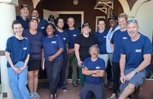 A group of twelve medical professionals from the UK Emergency Medical Team (UK EMT) posing in front of a building in Jamaica, all wearing blue shirts with the "UK-Med" logo.