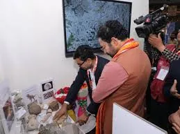 Union Minister G. Kishan Reddy examines geological samples at a GSI exhibition in Jaipur. A man in a suit points to samples on a table, while a camera operator films.