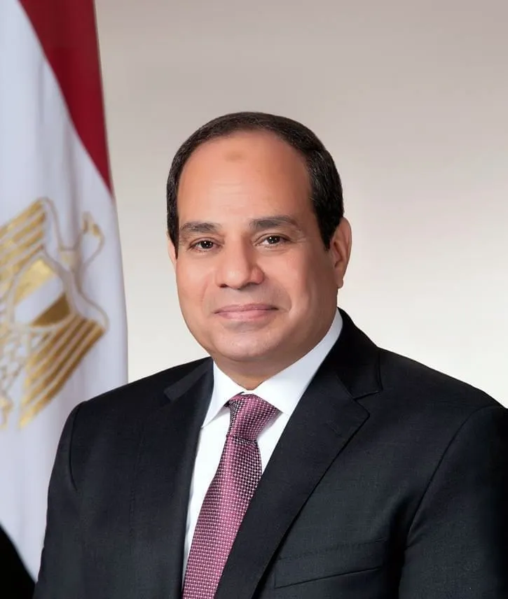 Portrait of Egyptian President Abdel Fattah El-Sisi in a dark suit and red tie, standing in front of an Egyptian flag.