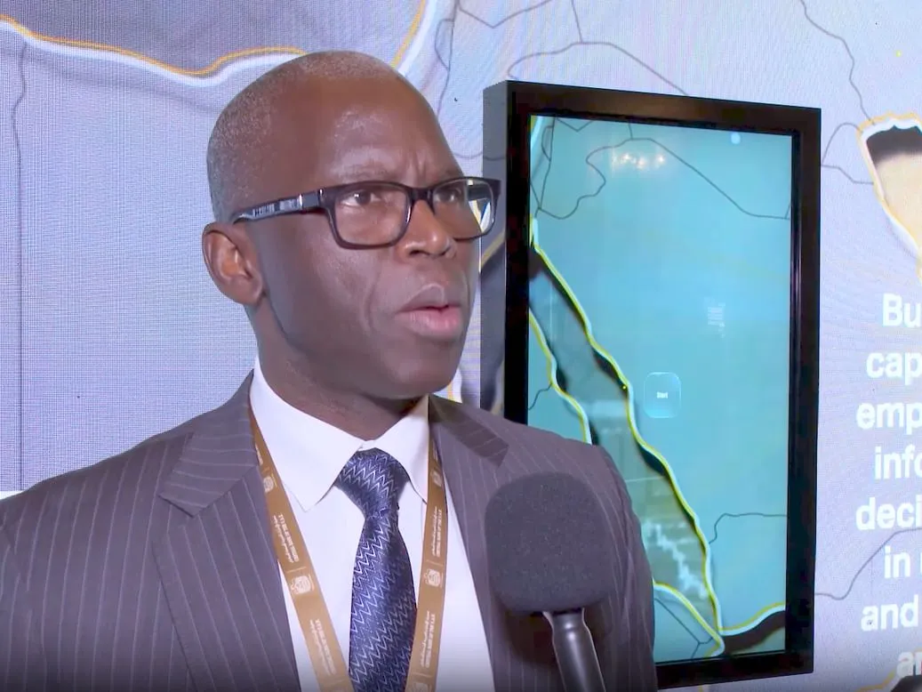 Ousmane Dione, Vice President for the World Bank's MENAAP region, speaks at the MENA Leaders' Summit on Financial Inclusion in Abu Dhabi, wearing glasses and a striped suit, with a digital display showing a map behind him.