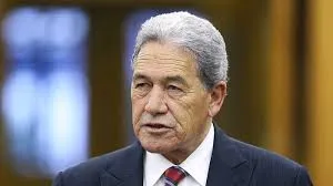 Head and shoulders shot of New Zealand Foreign Minister Winston Peters wearing a dark suit, white shirt, and a red and blue plaid tie.