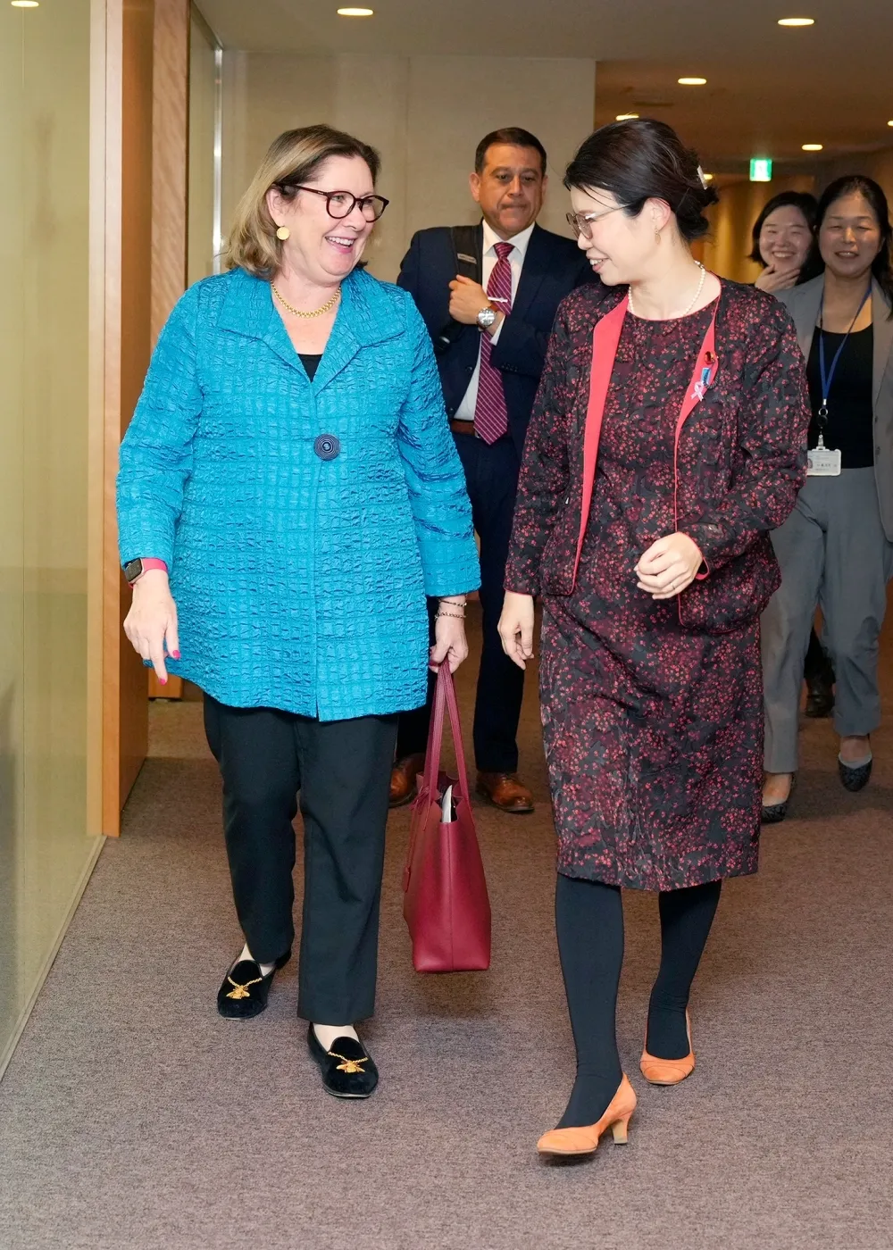 Japanese State Minister Kunimitsu Ayano in a floral outfit walks alongside MFO Director General Elizabeth Dibble in a blue jacket during a meeting in Tokyo