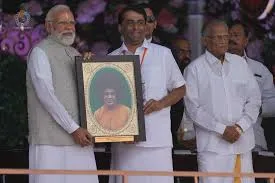 Prime Minister Narendra Modi holds a framed portrait of Sri Sathya Sai Baba alongside a Sri Sathya Sai Central Trust official during a felicitation ceremony at Prasanthi Nilayam in Puttaparthi, Andhra Pradesh.