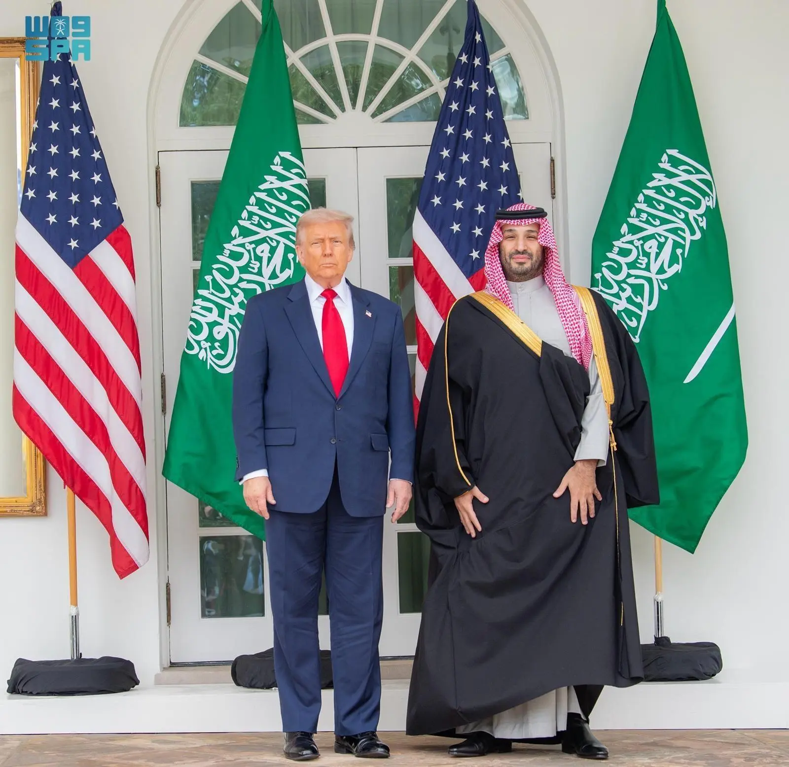 U.S. President Donald Trump and Saudi Crown Prince Mohammed bin Salman stand side-by-side in front of U.S. and Saudi flags at the White House entrance.