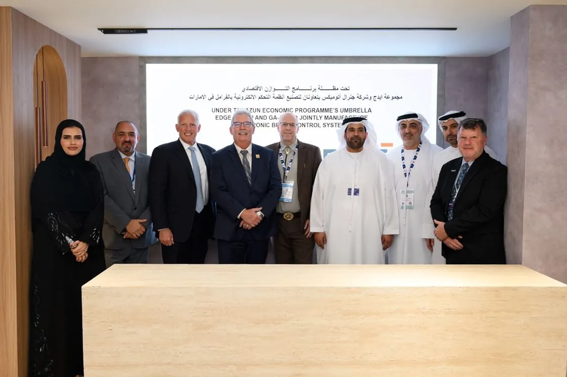 A group of nine representatives from Tawazun Council, EDGE Group’s EPI, and General Atomics standing together in a conference room in front of a screen announcing a joint manufacturing agreement.