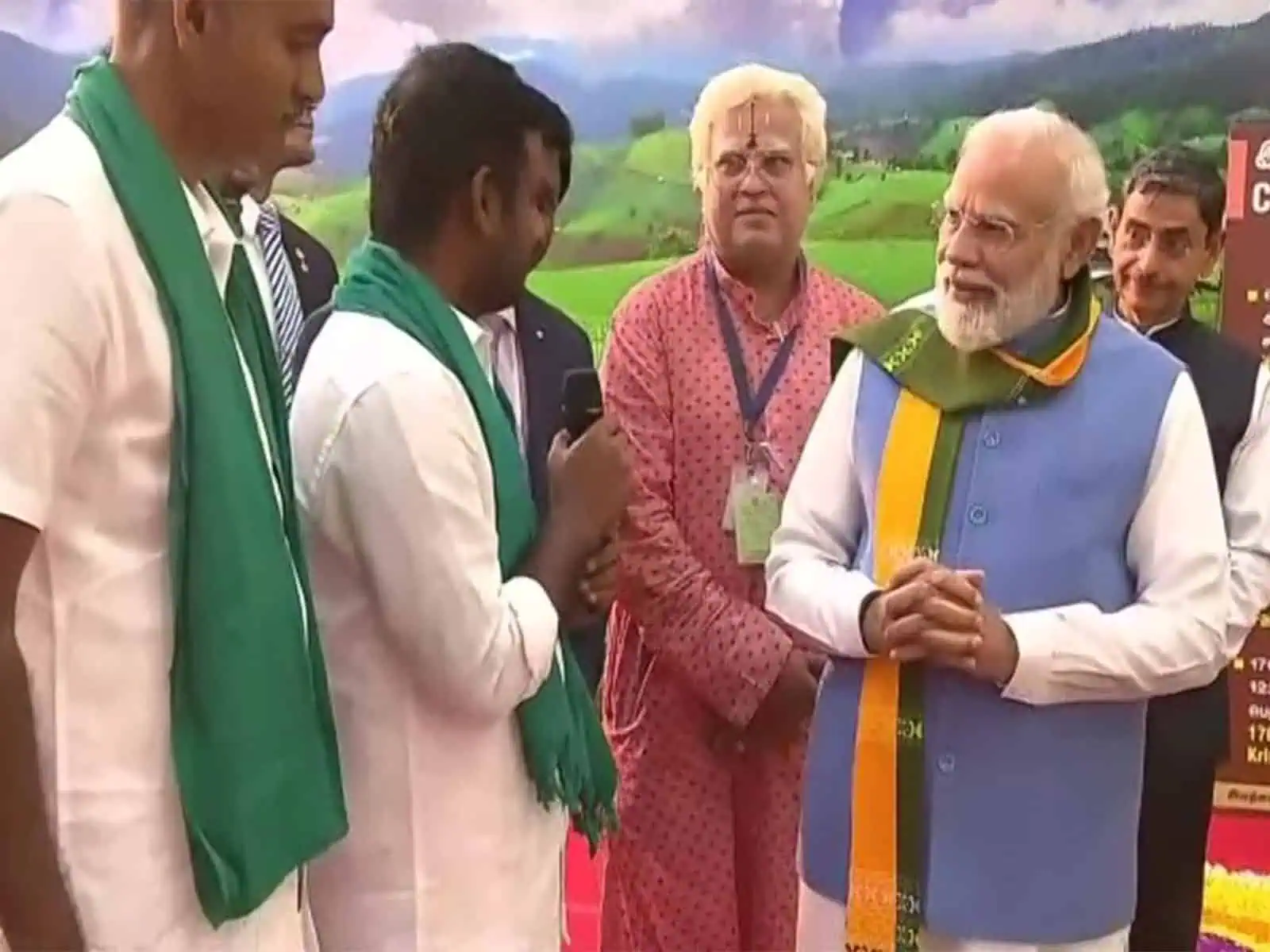 Prime Minister Narendra Modi listening to a young farmer speaking on a microphone during the South India Natural Farming Summit 2025 in Coimbatore, Tamil Nadu.
