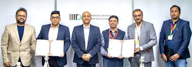 Officials from TEC and IIIT Delhi standing in a row holding signed MoU documents for telecom research collaboration against a branded backdrop.
