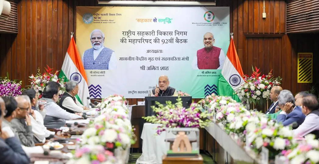 Union Home and Cooperation Minister Amit Shah addressing the 92nd General Council Meeting of the National Cooperative Development Corporation (NCDC) in New Delhi, seated at a conference table with a banner featuring PM Modi in the background.
