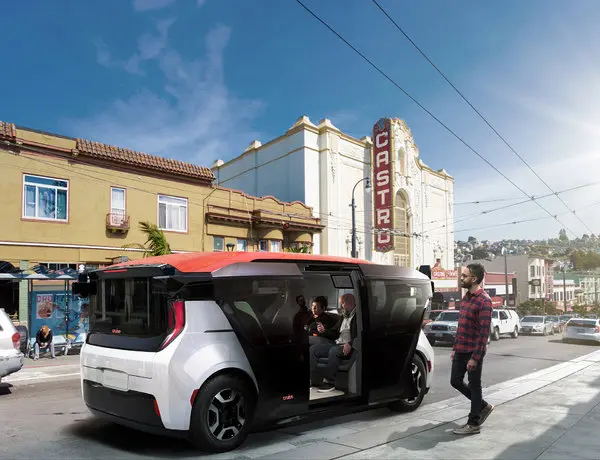 A white and orange Cruise Origin autonomous vehicle with sliding doors open, parked in front of the historic Castro Theatre in San Francisco, with passengers inside and a man standing nearby.