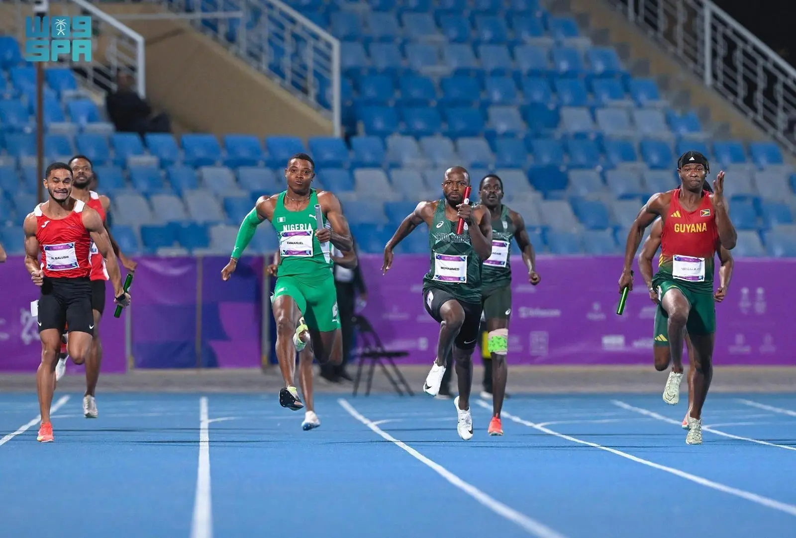 Saudi sprinter Mohammed races alongside athletes from Nigeria, Oman, and Guyana during the men's 4x100m relay final at the Islamic Solidarity Games in Riyadh.