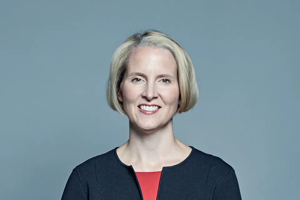 Official portrait of UK Environment Secretary Emma Reynolds smiling, wearing a black jacket and red top against a plain background.
