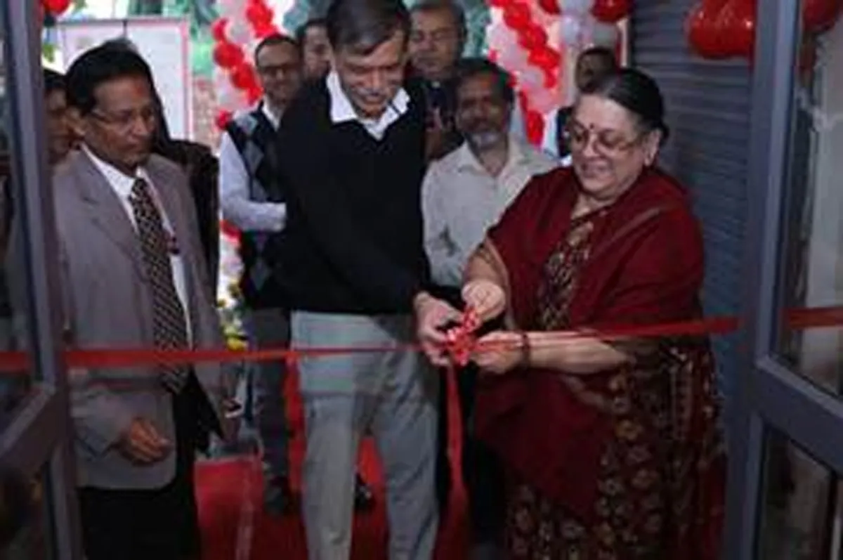 A woman in a maroon sari cuts a red ribbon to inaugurate the revamped Delhi University Post Office, flanked by officials and guests amidst festive red and white balloons.