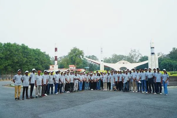 Group of National Space Day Quiz 2025 winners standing in front of the Satish Dhawan Space Centre entrance gate featuring rocket models in Sriharikota.