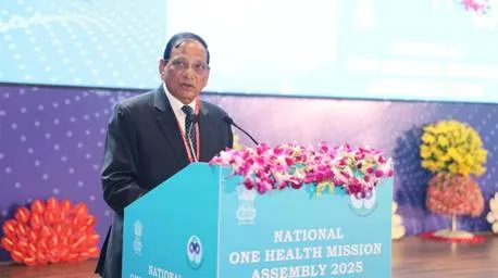 Union Health Minister J P Nadda addressing the National One Health Mission Assembly 2025 at Bharat Mandapam, standing behind a light blue podium decorated with flowers.