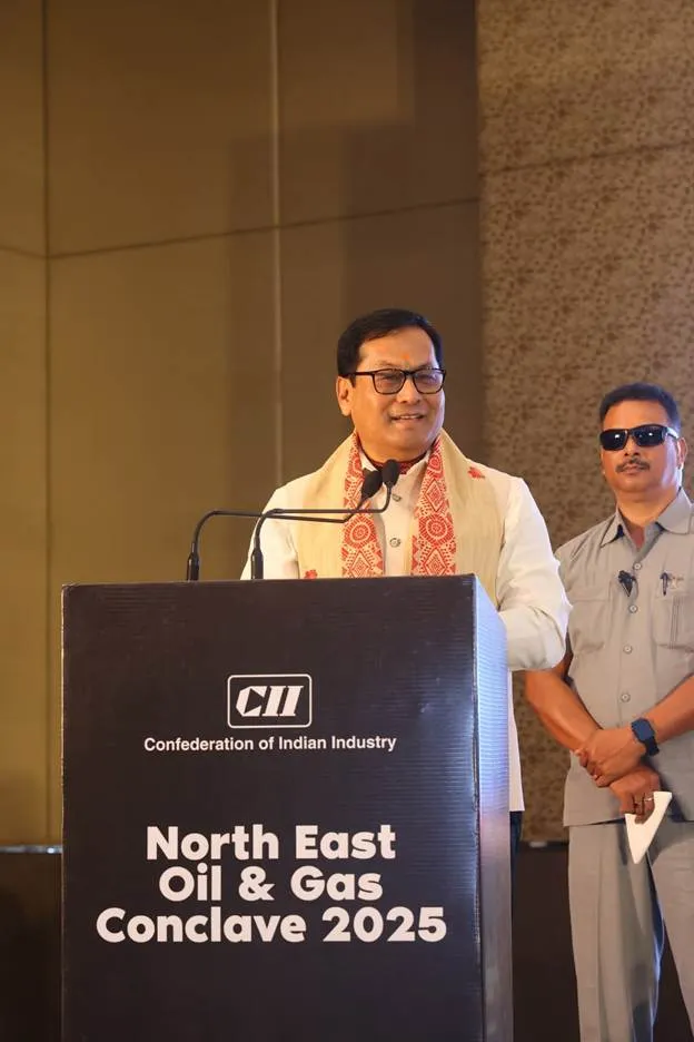 Union Minister Sarbananda Sonowal addressing the audience from a podium at the North East Oil & Gas Conclave 2025, wearing a traditional Assamese Gamosa.